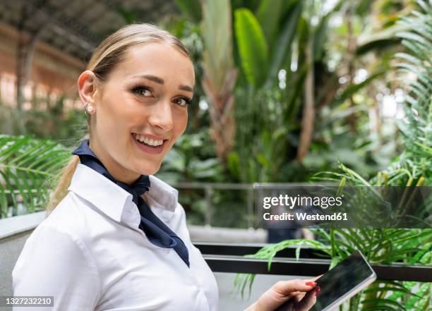 smiling air stewardess with digital tablet in garden - air stewardess stockfoto's en -beelden