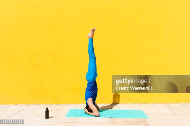 man practicing salamba shirshasana while doing yoga by yellow wall - shirshasana stock pictures, royalty-free photos & images