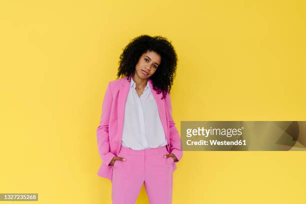 businesswoman with head cocked standing against yellow background - kopf zur seite neigen stock-fotos und bilder