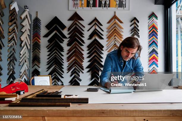 craftsman writing on notepad while leaning on table in workshop - computer store stockfoto's en -beelden