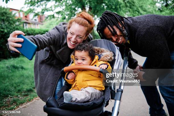cheerful parents taking selfie with son in stroller at park - carrinho de criança imagens e fotografias de stock