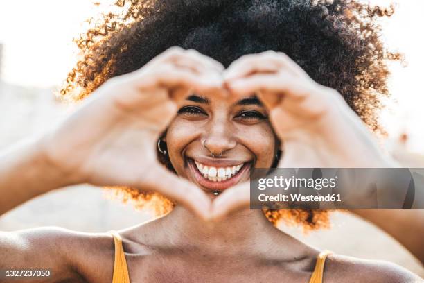 smiling woman with heart shape from hands at beach - herz hände stock-fotos und bilder