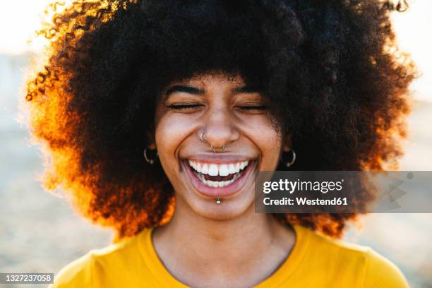 young afro woman laughing with eyes closed at beach - 鼻ピアス ストックフォトと画像