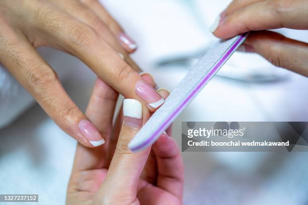 closeup shot of a woman in a nail salon receiving a manicure by a beautician with nail file. woman getting nail manicure. beautician file nails to a customer. - nagelhaut stock-fotos und bilder