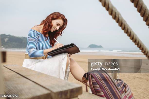 female professional using graphic tablet while sitting on steps at beach - graphics tablet stock pictures, royalty-free photos & images