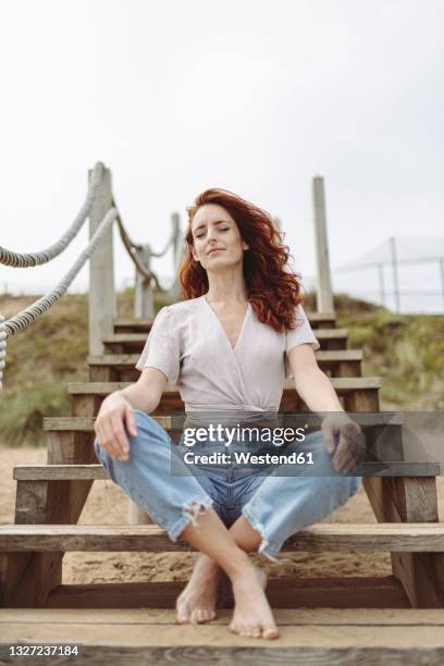 redhead woman meditating while sitting cross-legged on steps - barefoot redhead ストックフォトと画像