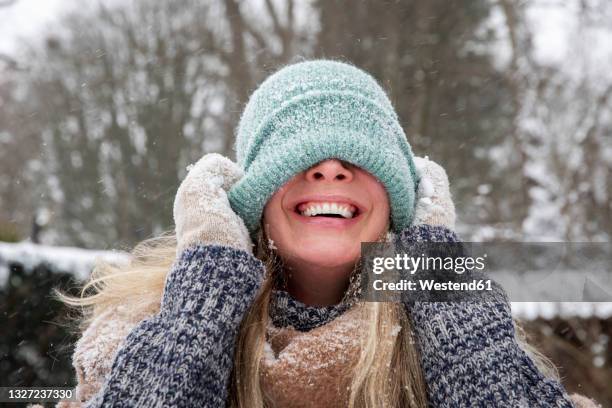 cheerful woman covering face with knit hat during winter - woman in a shawl stock-fotos und bilder