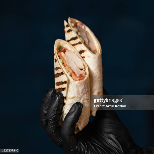 two halves of grilled shawarma on black background. stuffed pita bread in chef hand in black glove. close up shot - lavash stock pictures, royalty-free photos & images