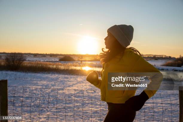 mature woman wearing knit hat running during winter - winter sport stock-fotos und bilder