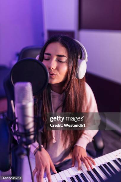 female musician singing through microphone while playing piano in studio - pianist front fotografías e imágenes de stock