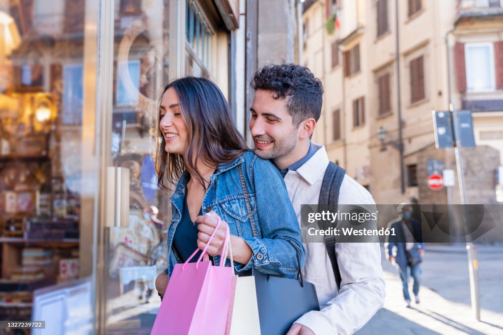 Smiling tourist couple window shopping while standing by store