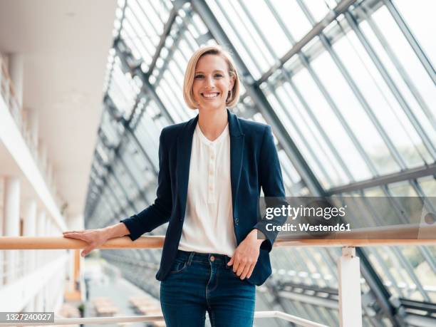 businesswoman smiling while standing by railing in office - blazer stockfoto's en -beelden