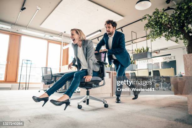 businessman playing with colleague sitting on office wheel chair - bürostuhl stock-fotos und bilder