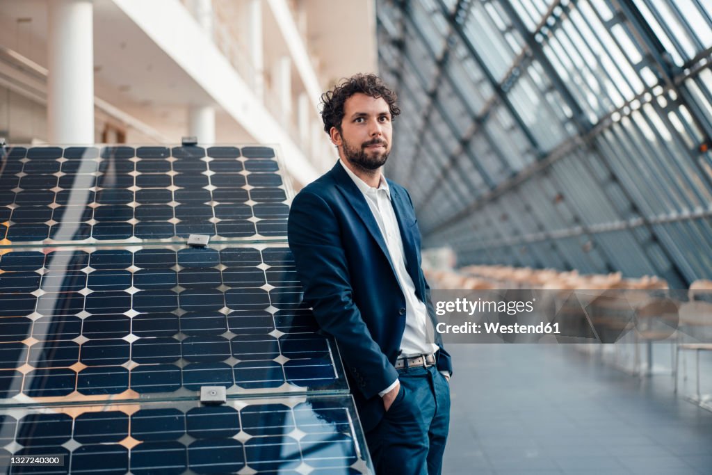 Businessman with hands in pockets leaning on solar panel