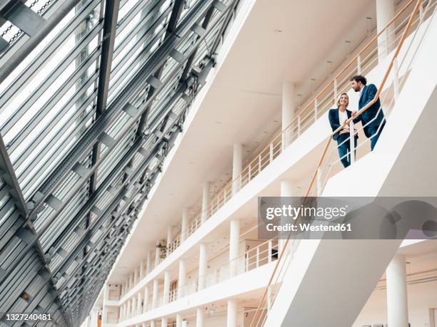 male and female entrepreneur having discussion while standing in staircase - business stairs stock-fotos und bilder