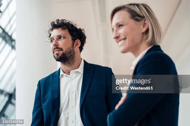 thoughtful male entrepreneur looking away while standing by colleague in office - distrarre lo sguardo foto e immagini stock