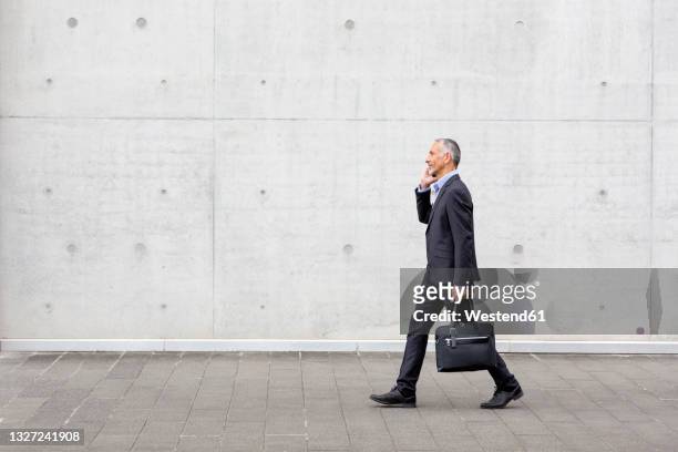 male professional with briefcase walking while talking on smart phone - phone side view stock pictures, royalty-free photos & images