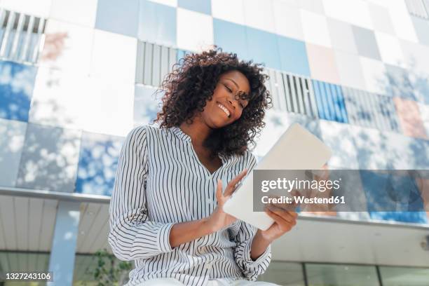 cheerful curly haired businesswoman using digital tablet while sitting in front of office building - person in front of computer stock pictures, royalty-free photos & images