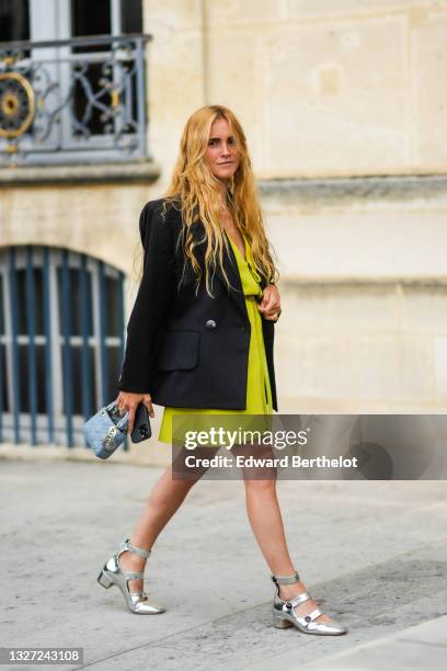 Blanca Miro wears a gold pendant chain necklace, a yellow V-neck zipper large short dress, a yellow shiny leather with red heart print pattern belt,...