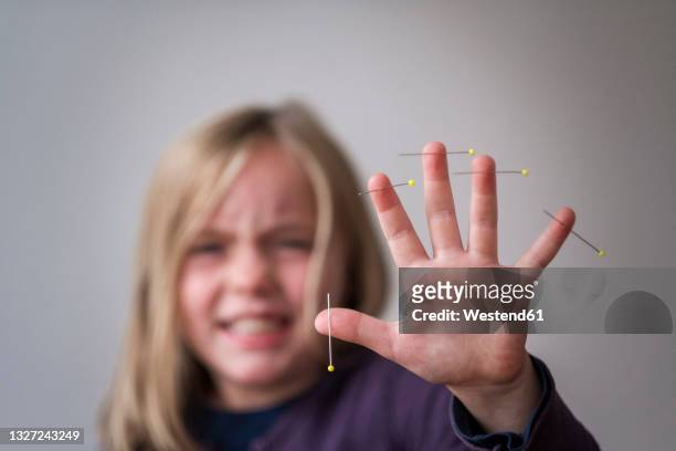 girl showing hand with pins pierced in skin against gray background - pin up girl stockfoto's en -beelden