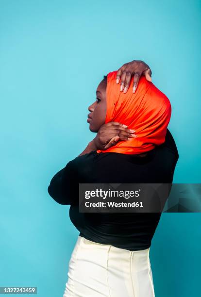 woman looking away in front of blue background - hijab woman from behind stock pictures, royalty-free photos & images