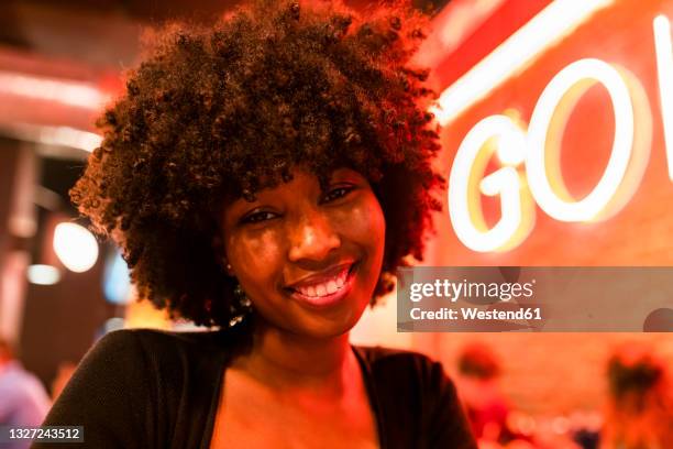 smiling afro woman with neon lighting on face at bar - neon lighting smiling stock pictures, royalty-free photos & images