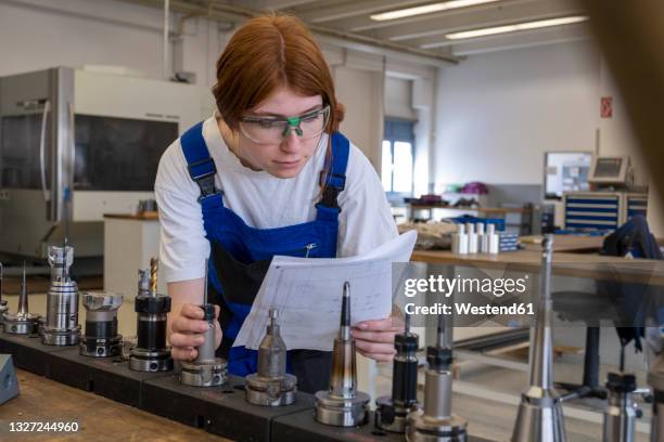 female technician working with metallic machinery parts while reading book at workshop - mechatronics fotografías e imágenes de stock