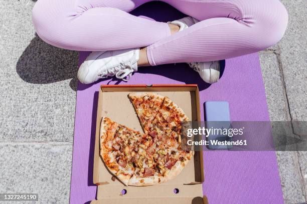 female athlete sitting cross-legged in front of pizza on exercise mat - open workout stockfoto's en -beelden