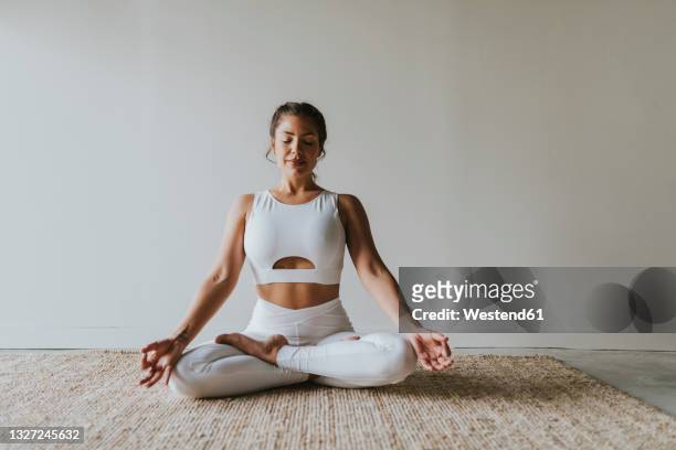 female fitness teacher meditating in lotus position at yoga studio - yoga stock-fotos und bilder