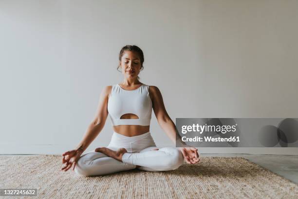 female fitness teacher meditating in lotus position at yoga studio - mediteren stock-fotos und bilder