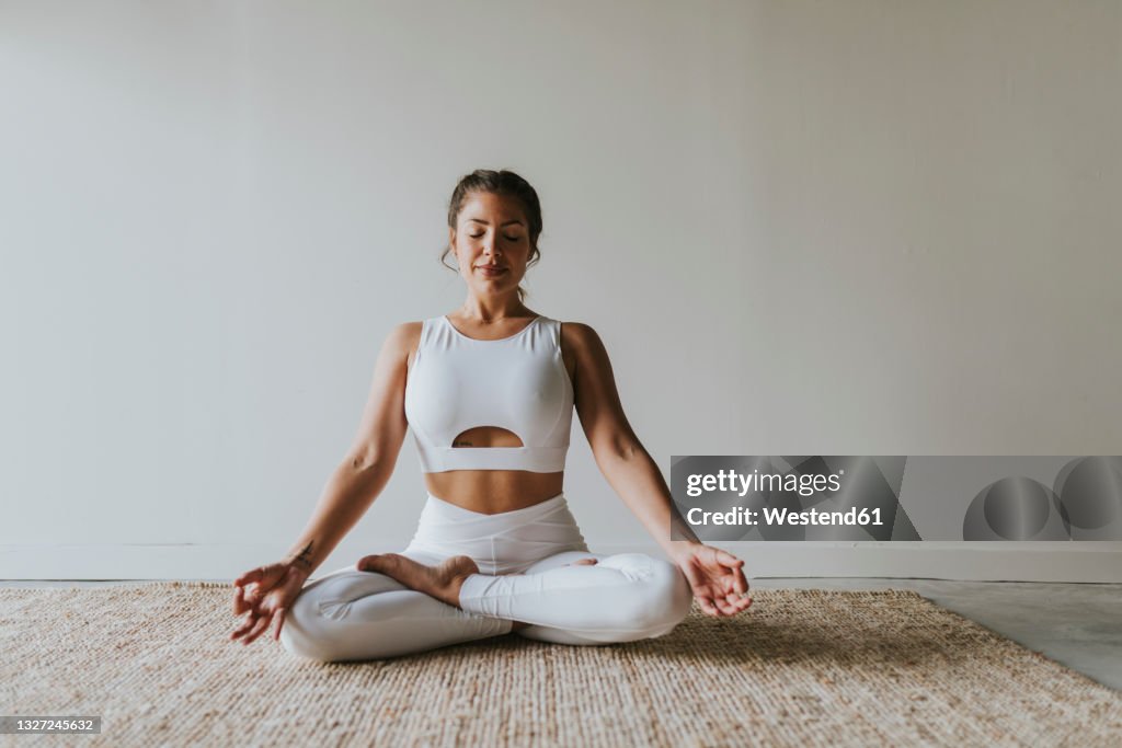 Female fitness teacher meditating in lotus position at yoga studio
