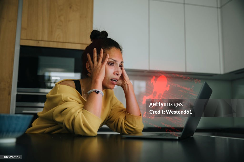 Woman with head in hands looking at danger icon laptop