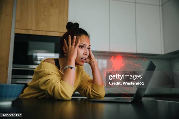 woman with head in hands looking at danger icon laptop - phishing stock pictures, royalty-free photos & images