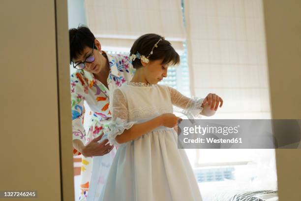 mother helping daughter getting dressed for communion at home - dresssing stock pictures, royalty-free photos & images