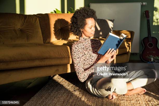 woman reading book while sitting cross-legged at home - book reading fotografías e imágenes de stock