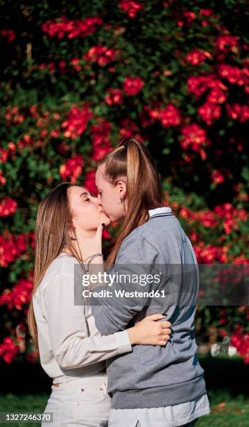 women kissing while standing in front of flowering plant at park - photos of lesbians kissing stock pictures, royalty-free photos & images