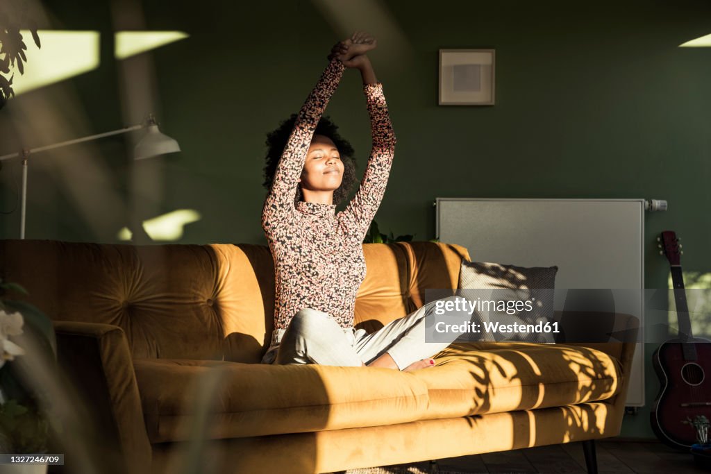 Woman with hands raised sitting on sofa at home