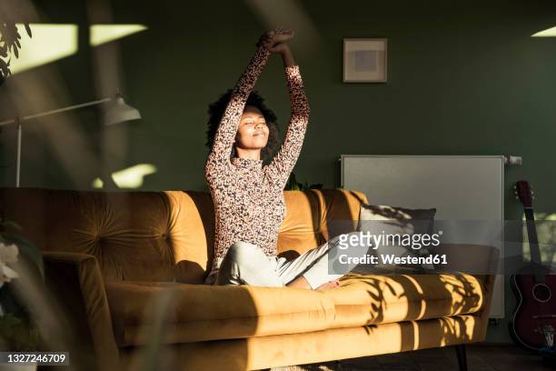 woman with hands raised sitting on sofa at home - relaxation stock pictures, royalty-free photos & images