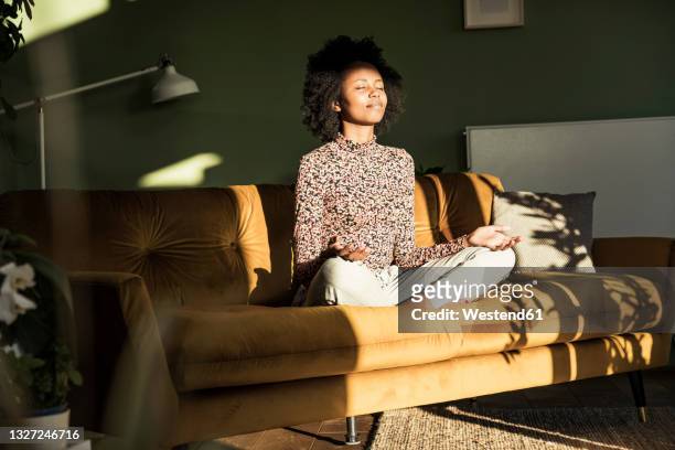 woman meditating while sitting on sofa at home - meditation stock pictures, royalty-free photos & images