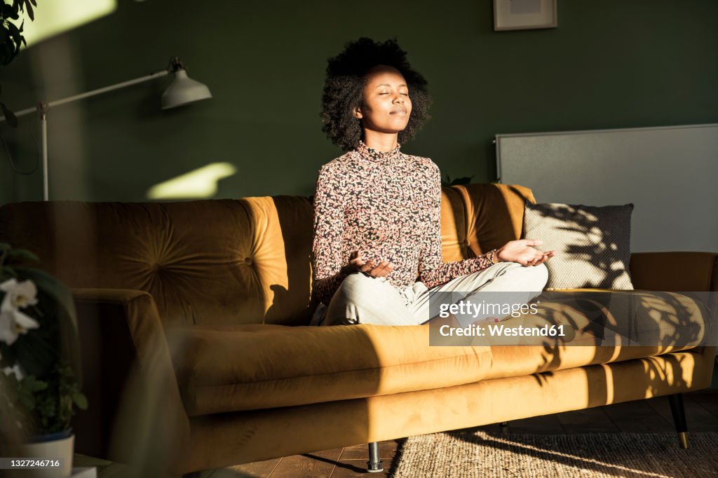 Woman meditating while sitting on sofa at home