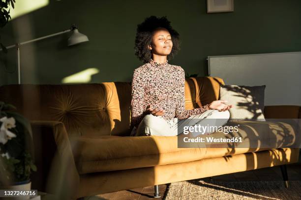 woman meditating while sitting on sofa at home - bem estar mental imagens e fotografias de stock