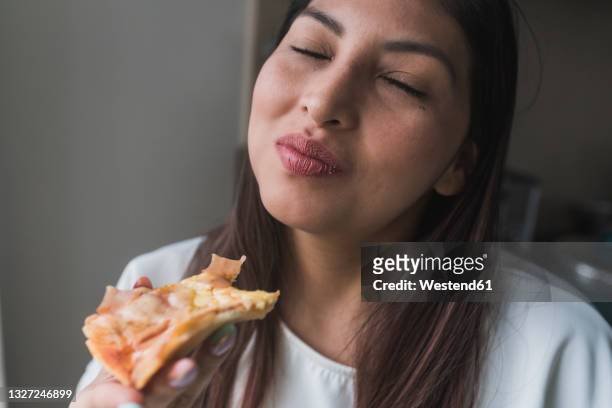 woman with eyes closed eating pizza at home - soddisfazione foto e immagini stock