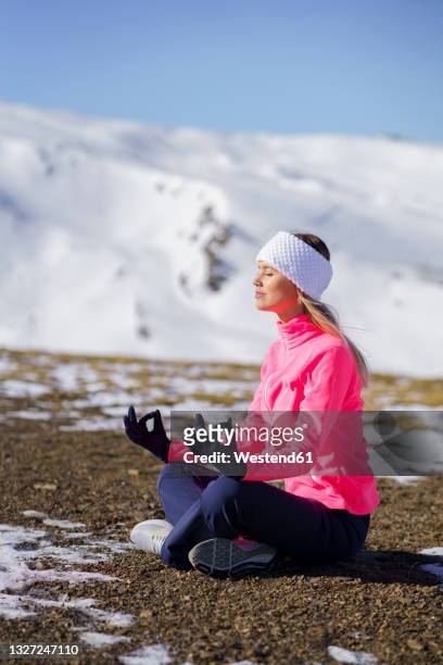 sportswoman meditating in lotus position on sunny day - yoga in the snow stock-fotos und bilder