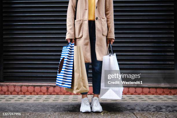 woman holding shopping bags in front of closed shutter - einkaufstüte stock-fotos und bilder