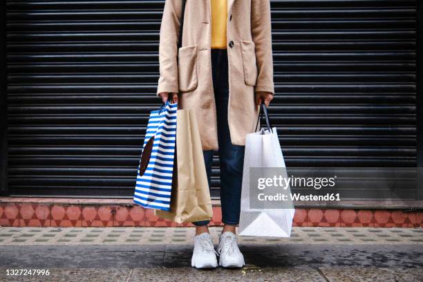 woman holding shopping bags in front of closed shutter - purchase imagens e fotografias de stock