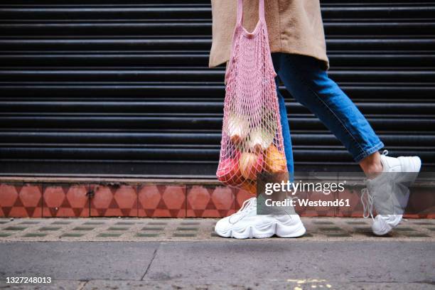 woman with fruits in mesh bag walking by shutter - food close up stock pictures, royalty-free photos & images
