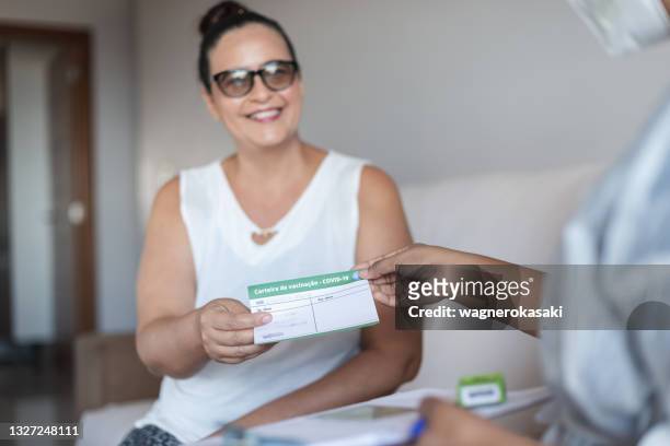 vaccination at home. mature woman receiving her vaccination record card ("carteira de vacinação", written in portuguese) from nurse - vacinação stockfoto's en -beelden