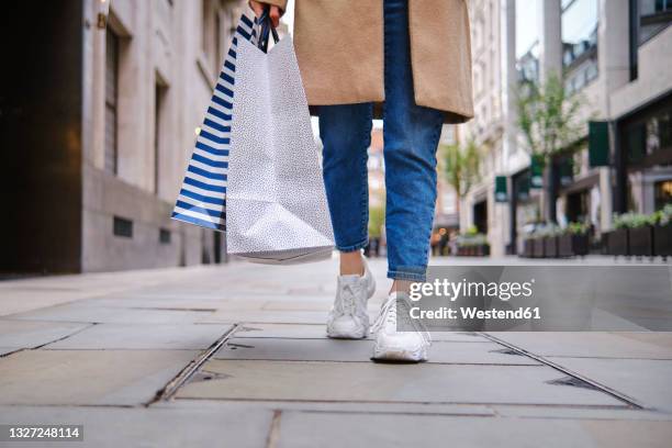 woman with shopping bags walking on footpath - überzieher stock-fotos und bilder