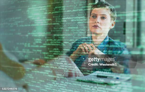 female professional looking at binary codes on glass at office - digitalisering bildbanksfoton och bilder