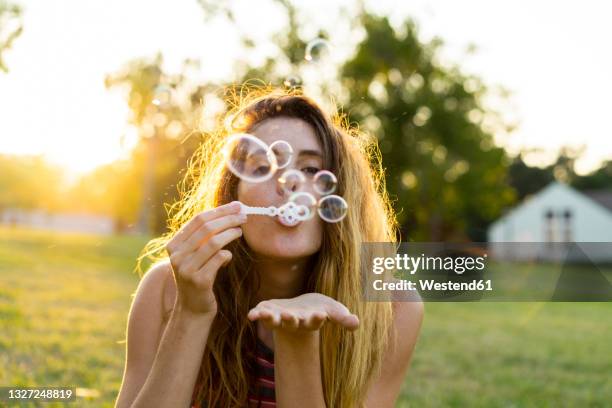 young woman blowing bubbles at park - froth stock-fotos und bilder